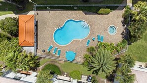 Eine Vogelperspektive eines Hotels mit Swimmingpool, Liegestühlen und Palmen.