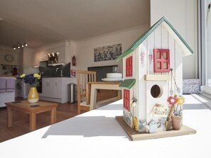 Une nichée à oiseaux avec une pancarte sur laquelle on peut lire « Bienvenue », posée sur une table dans une pièce où l’on aperçoit une cuisine au fond.