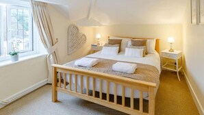 Een slaapkamer met een houten bed, nachtlampjes, een wanddecoratie in de vorm van een hart en een raam met gordijnen.