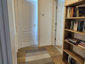 A hallway with a striped rug, a bookshelf with books, and a closed door. - 2 Bed in Ilfracombe (oc-87979) (Ilfracombe)