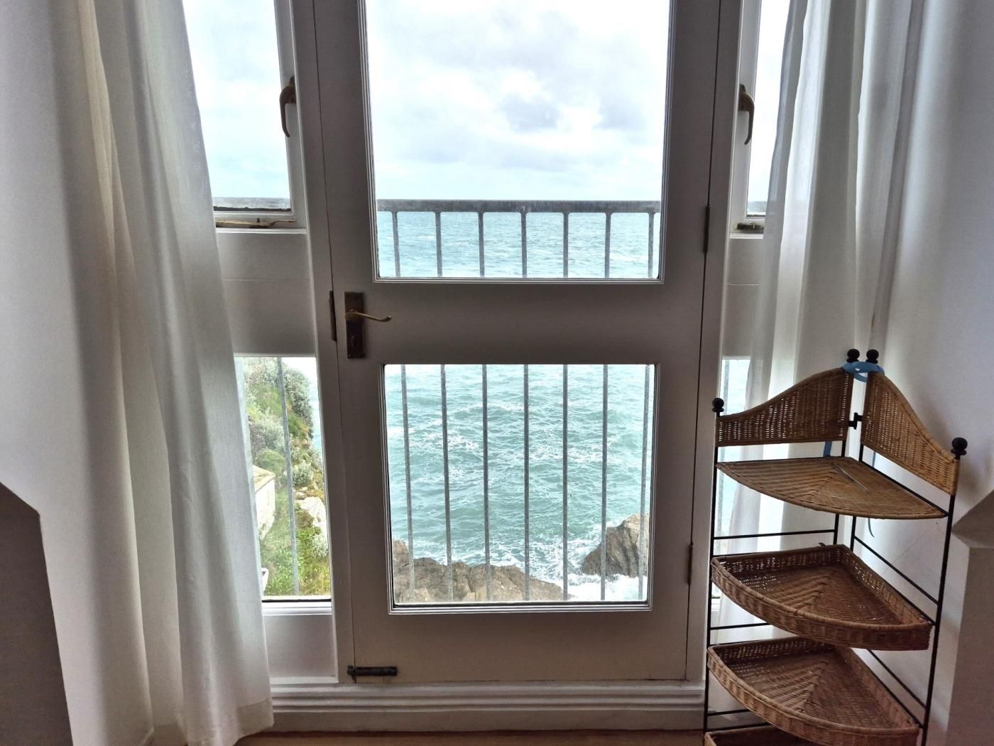 A room with a large window overlooking the sea, a wicker shelf, and a door with a handle.