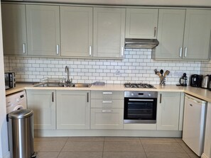 A modern kitchen with light-colored cabinets, a stainless steel sink, a gas stove, and a built-in oven. - 2 Bed in Ilfracombe (oc-87979) (Ilfracombe)