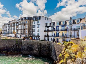 A coastal town with multi-story buildings, a stone wall, and a body of water. - 2 Bed in Ilfracombe (oc-87979) (Ilfracombe)