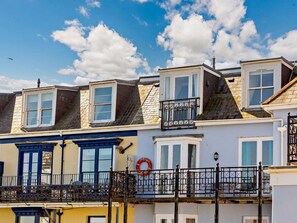 A row of terraced houses with dormer windows, a balcony with a railing, and a wreath on the wall. - 2 Bed in Ilfracombe (oc-87979) (Ilfracombe)