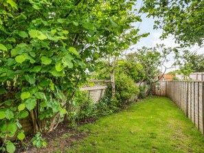A fenced backyard with a grassy area and dense foliage. - 2 Bed in Norwich (oc-88326) (Bacton)