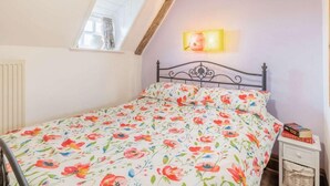 Une chambre à coucher comprenant un lit, une table de chevet, une lampe, une fenêtre et des poutres apparentes.