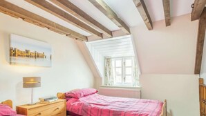 Une chambre avec deux lits, une fenêtre avec des rideaux, un radiateur et un tableau représentant un paysage urbain.