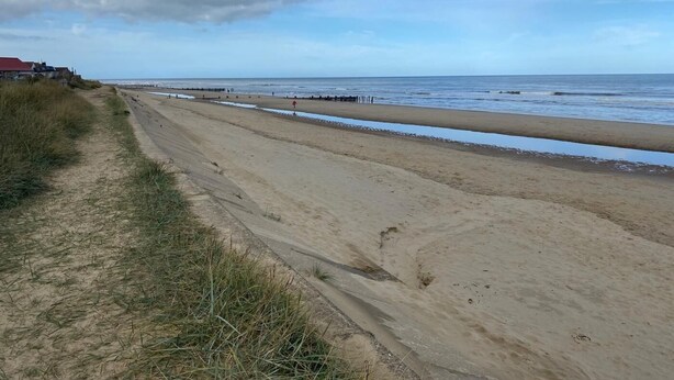 Une plage de sable fin, avec un ciel dégagé et quelques nuages.
