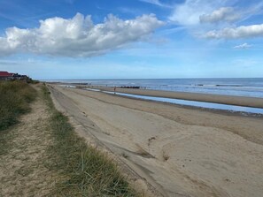 Ein Sandstrand mit blauem Himmel und vereinzelten Wolken.