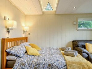 A bedroom with a wooden bed, two bedside lamps, a window, and a leather sofa.