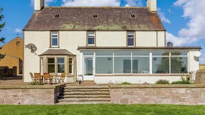 A two-story house with a large glass bay window, a stone staircase leading to the entrance, and a small porch with outdoor seating. - 4 Bed in Brechin (oc-89698) (Brechin)