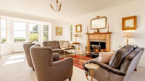 A spacious living room with a fireplace, large windows, and classic furniture. - 4 Bed in Brechin (oc-89698) (Brechin)
