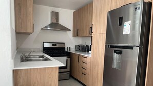 Una cocina compacta con refrigerador de acero inoxidable, horno empotrado, microondas y armarios de madera.