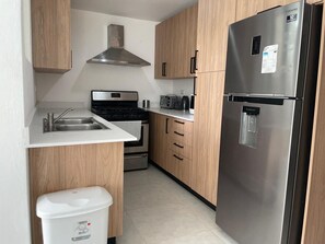 Eine kompakte Küche mit Edelstahl-Kühlschrank, Backofen, Mikrowelle und Holzschränken.