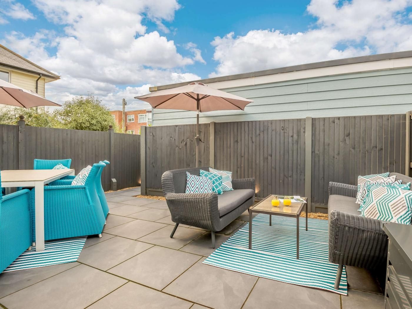 A patio with outdoor furniture, a table, and a striped rug.