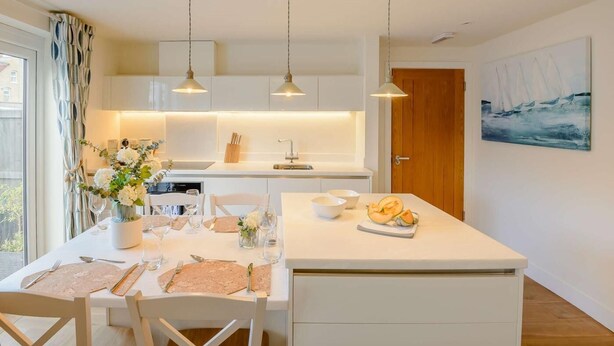 Una cucina moderna con luci a sospensione, un tavolo da pranzo apparecchiato per due persone e un quadro appeso al muro.