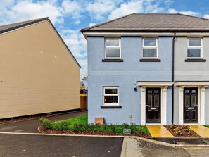 A two-story residential building with a garage, a front entrance with a door, and a small garden area with plants. - 2 Bed in Appledore (oc-90648) (Appledore)