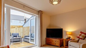 A living room with a TV, sofa, and a view of an outdoor patio. - 2 Bed in Appledore (oc-90648) (Appledore)