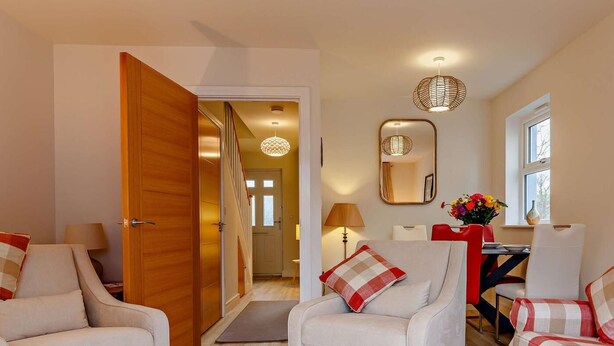 A modern living room with a wooden door, two armchairs, a sofa, a dining table with chairs, a mirror, and a hanging light fixture. - 2 Bed in Appledore (oc-90648) (Appledore)