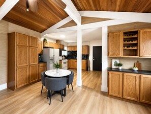 Eine moderne Küche mit Holzausbau, einer zentralen Kochinsel mit Sitzgelegenheiten und einer schwarzen Tür im Hintergrund.
