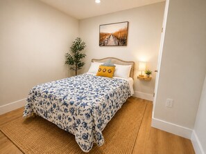 Ein Schlafzimmer mit einem Bett, einem Nachttisch mit Lampe, einem Wandbild und einer Topfpflanze.