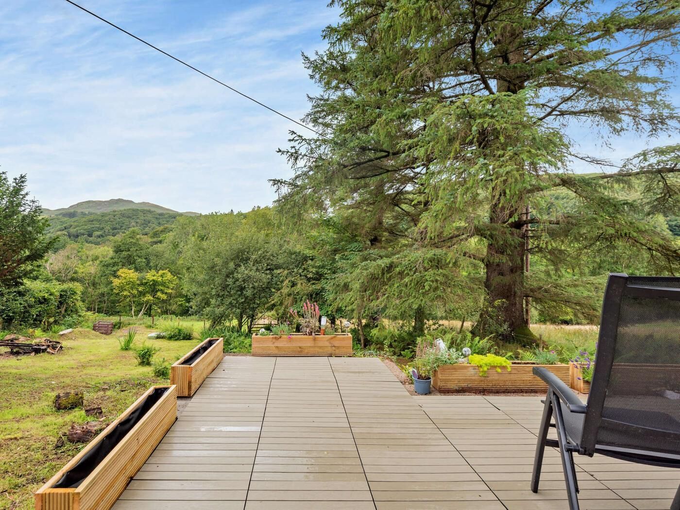 A wooden deck with built-in planters, a black outdoor chair, and a large tree in the background.