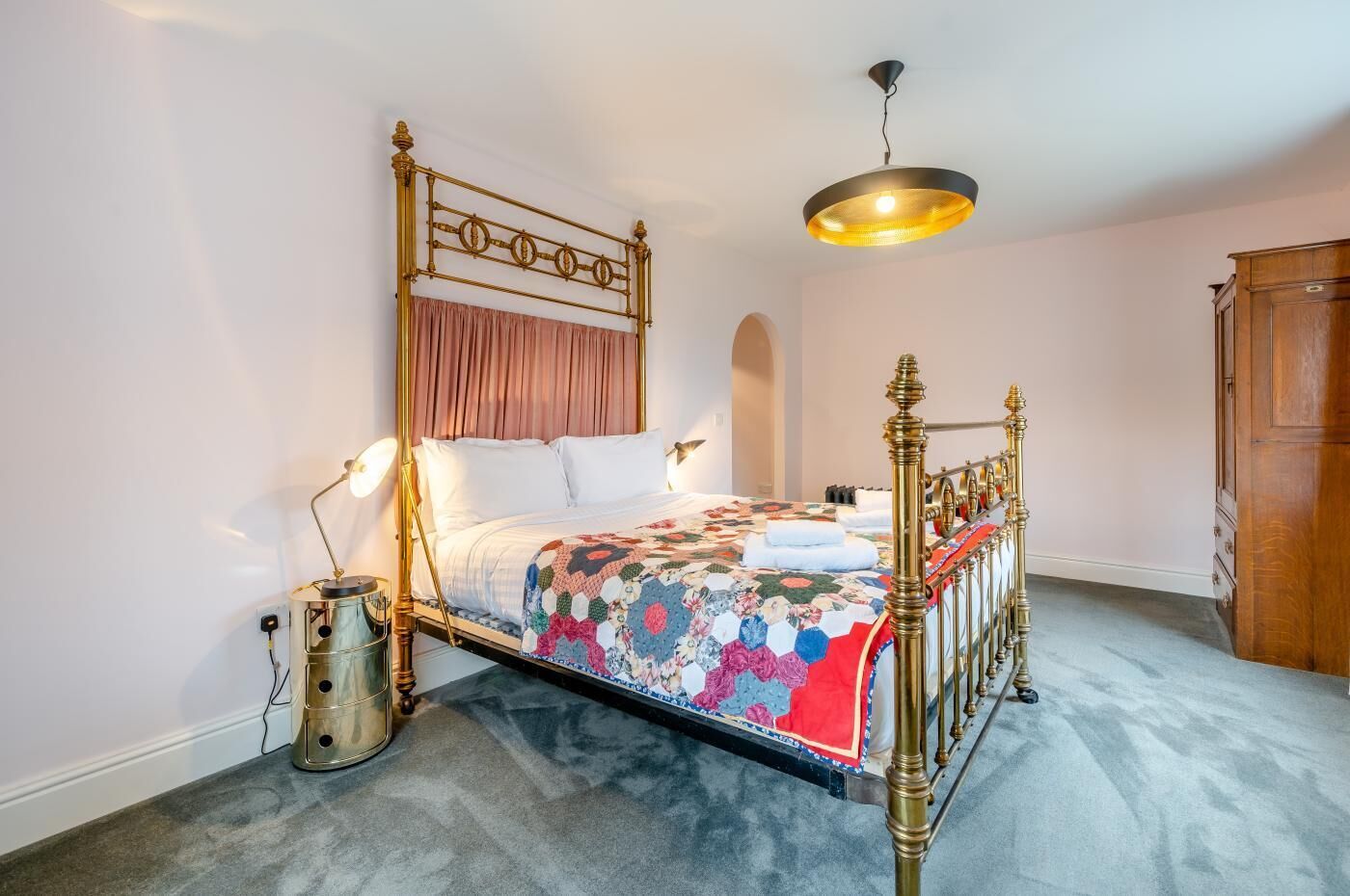 A bed with a gold frame, a quilt, and a hanging light fixture.