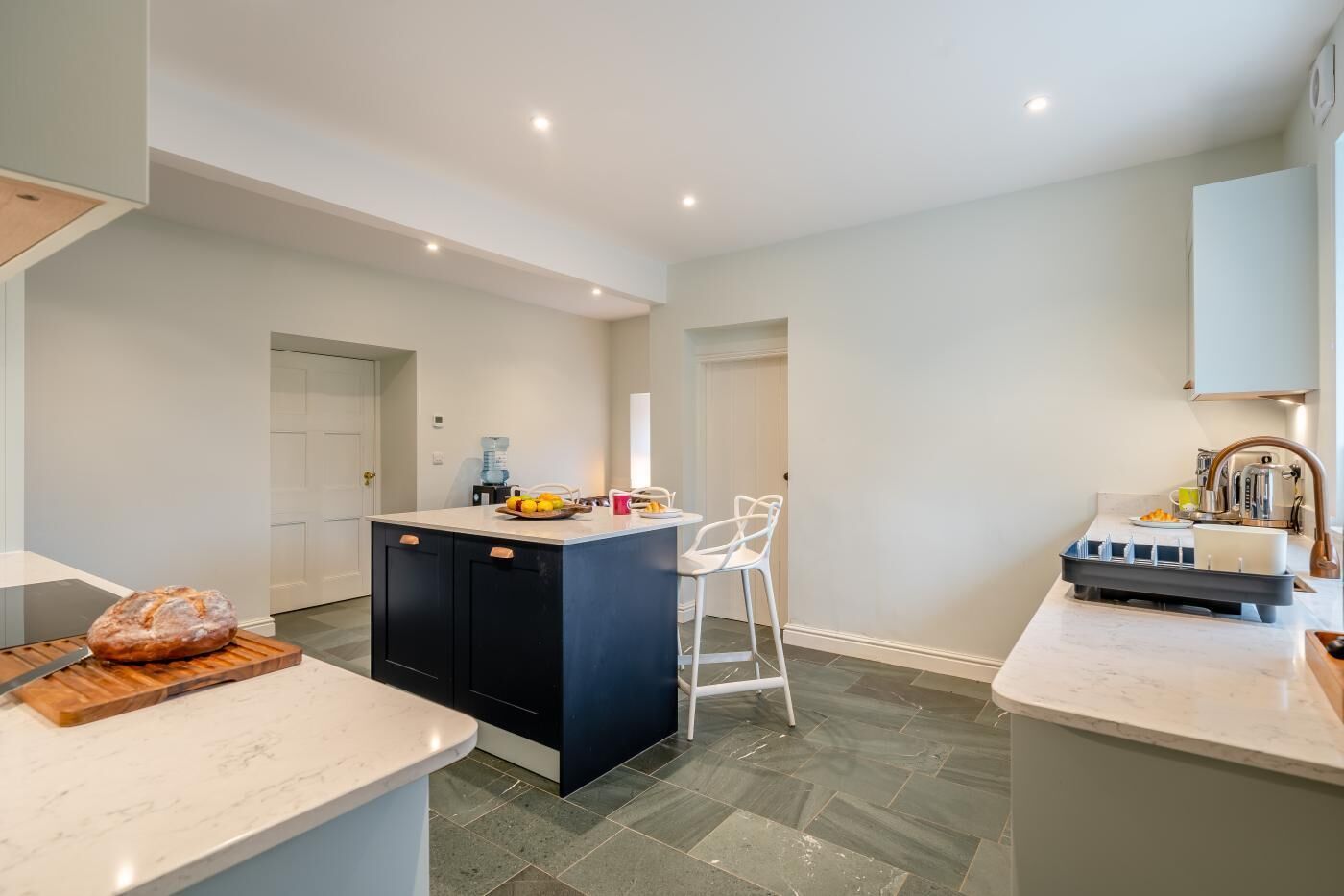 A modern kitchen with a central island, white bar stools, and a water dispenser.