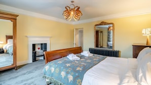 A hotel room with a large bed, a fireplace, a mirror, and a chandelier. - 3 Bed in Broughton-in-furness (oc-91862) (Broughton Mills)