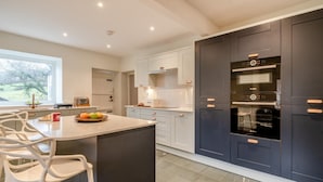 A modern kitchen with a central island, a Bosch oven, and a window with a view of trees. - 3 Bed in Broughton-in-furness (oc-91862) (Broughton Mills)