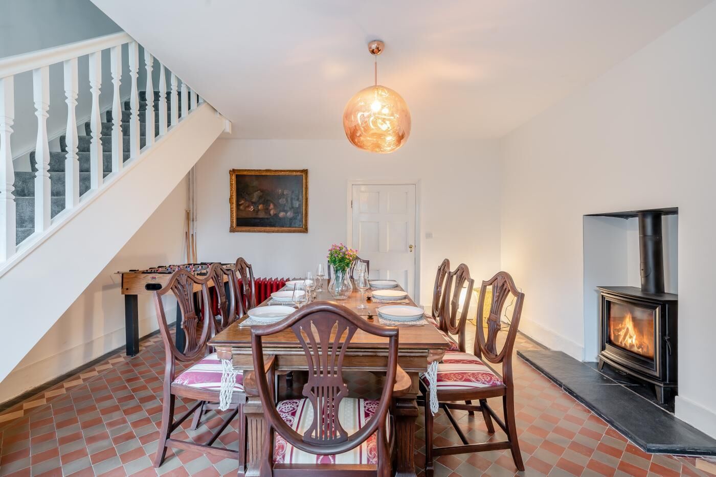 A dining room with a wooden table set for six, a fireplace, and a staircase.