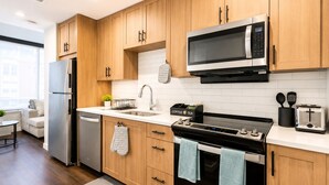 A modern kitchen with wooden cabinets, a stainless steel refrigerator, a microwave, a stove, and a toaster. - The Skyline Suite Midtown (Atlanta)