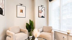 A modern room with two beige armchairs, a glass coffee table with decorative items, and framed artwork on the walls. - The Skyline Suite Midtown (Atlanta)