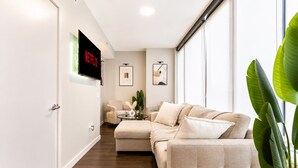 A modern living room with a beige sofa, a coffee table, and a TV mounted on the wall. - The Skyline Suite Midtown (Atlanta)