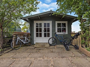 A small house with a porch, two bicycles, and a wooden fence.