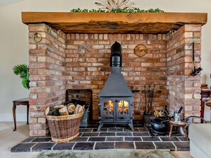 A stone fireplace with a black stove, logs, and a basket of firewood.