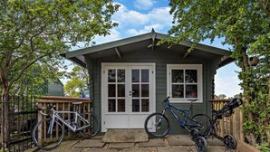 Uma pequena casa com varanda, duas bicicletas e cerca de madeira.