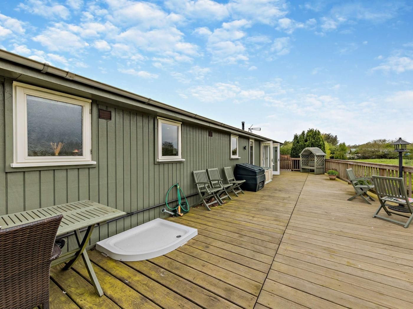 A deck with outdoor furniture, a hot tub, and a wooden deck extending from a building with windows.
