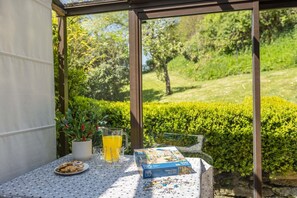 Ein Tisch mit einem Knobelkästchen, einer Teller Kekse und Gläser Orangensaft in einem überdachten Außenbereich mit Blick auf einen Garten.