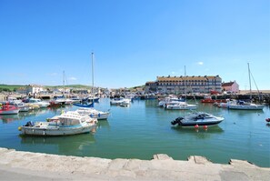 Ein Hafen mit verschiedenen Schiffen, ein großes Gebäude im Hintergrund und ein klarer, blauer Himmel.