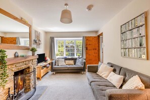 Ein gemütliches Wohnzimmer mit Kamin aus Stein, einem grauen Sofa und einem Bücherregal.