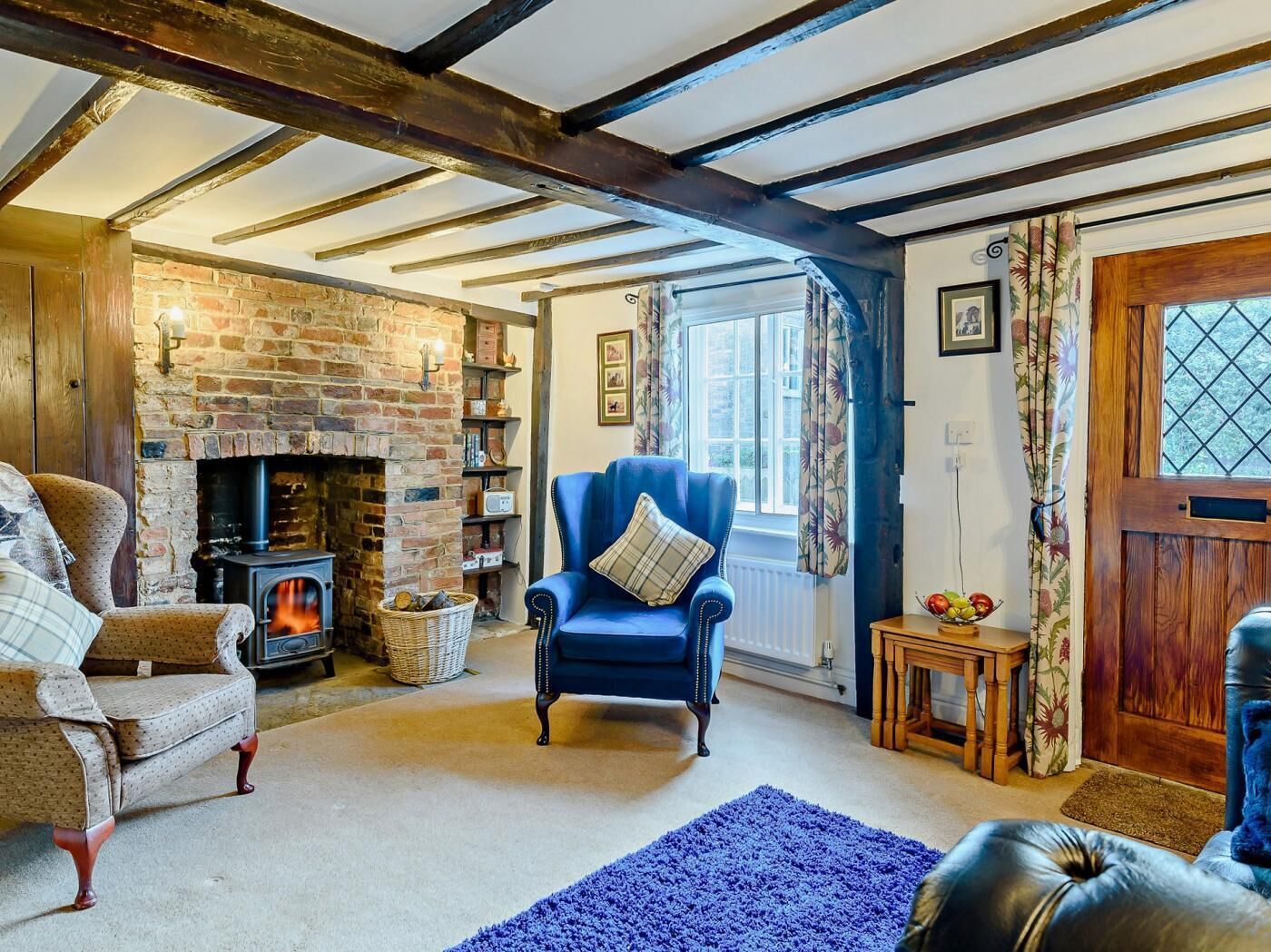 A cozy room with exposed wooden beams, a brick fireplace, a blue armchair, and a traditional wooden door.