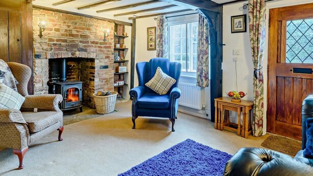 A cozy room with exposed wooden beams, a brick fireplace, a blue armchair, and a traditional wooden door. - 2 Bed in Horncastle (oc-93375) (Belchford)