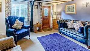 A room with a blue armchair, a leather sofa, a wooden door, and a framed picture on the wall. - 2 Bed in Horncastle (oc-93375) (Belchford)