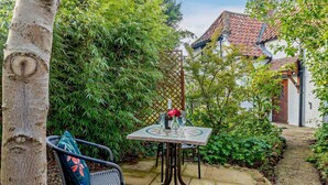 A patio with a table and chairs, surrounded by greenery and a building with a tiled roof. - 2 Bed in Horncastle (oc-93375) (Belchford)