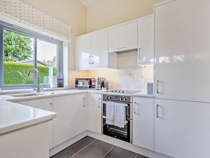 A modern kitchen with white cabinetry, a built-in oven, and a window with a view of greenery.