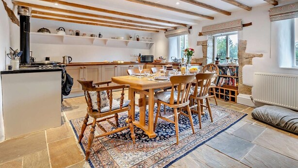Cocina rústica con vigas a la vista, una isla central y un comedor con sillas de madera y un tapete estampado.