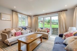 A living room with two sofas, a coffee table, and a view of a garden through large windows. - 5 Bed in Matlock (oc-93585) (Brassington)