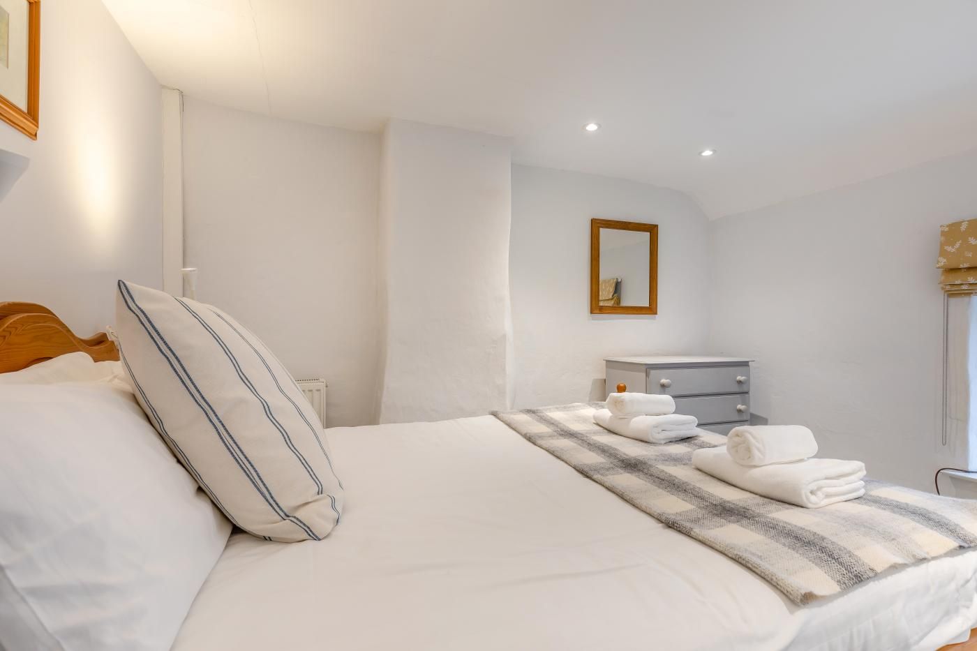 Habitación de hotel con cama, mesita de noche con toallas, cómoda y espejo en la pared.