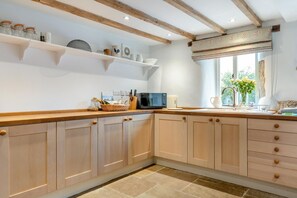 A kitchen with wooden cabinets, a microwave, and a window with flowers. - 5 Bed in Matlock (oc-93585) (Brassington)